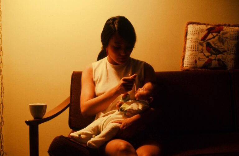 Mãe sentada no sofá à noite, com o bebê no colo, sob luz baixa