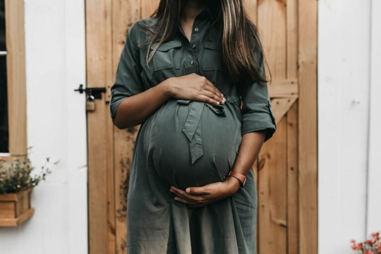 Gestante com as mãos na barriga diante de uma porta de madeira