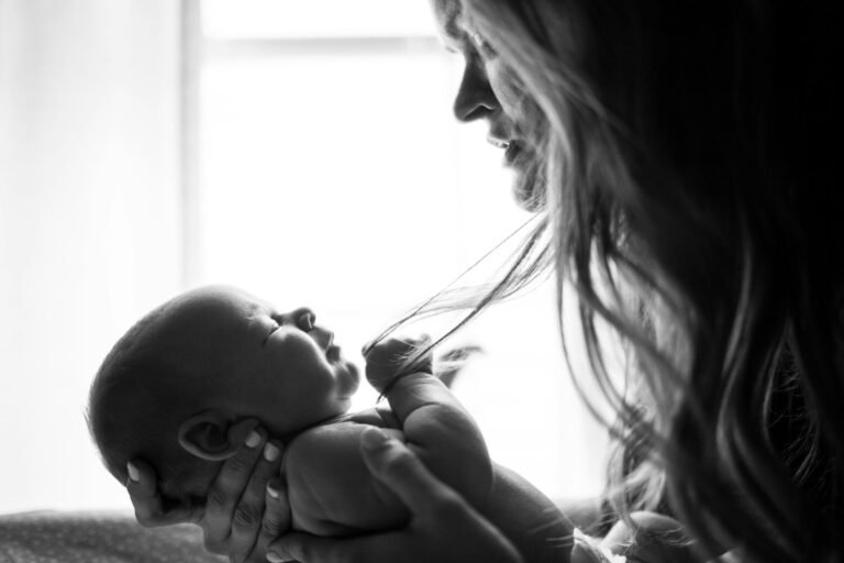 Mãe olhando para o bebê, que segura o dedo dela, em preto e branco